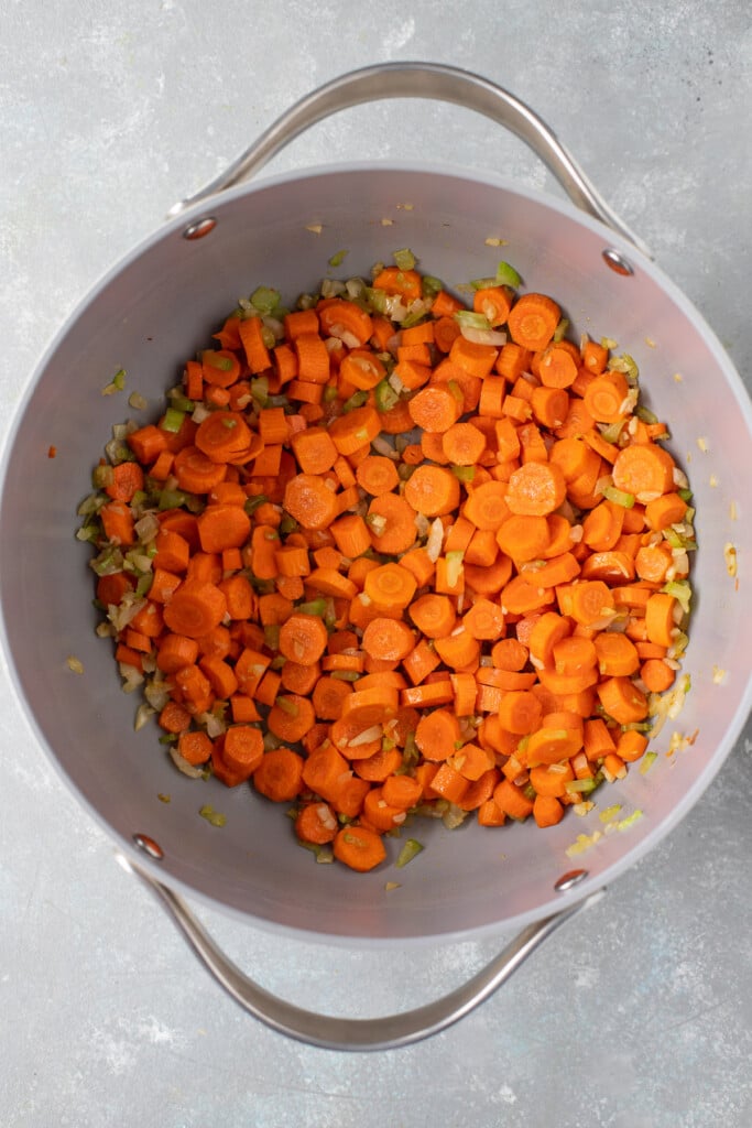 Carrots, onions, and celery in a grey pot on a grey background cooking to make turmeric chicken soup