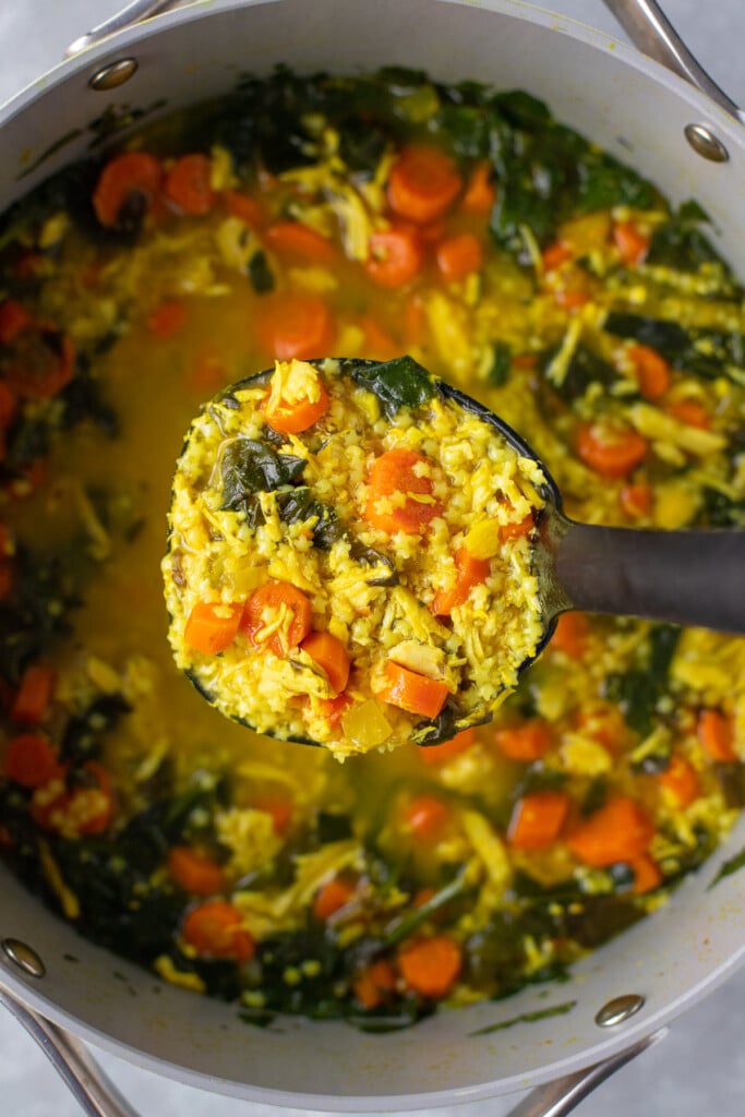 A ladle taking a large scoop out of a pot of lemon turmeric chicken soup