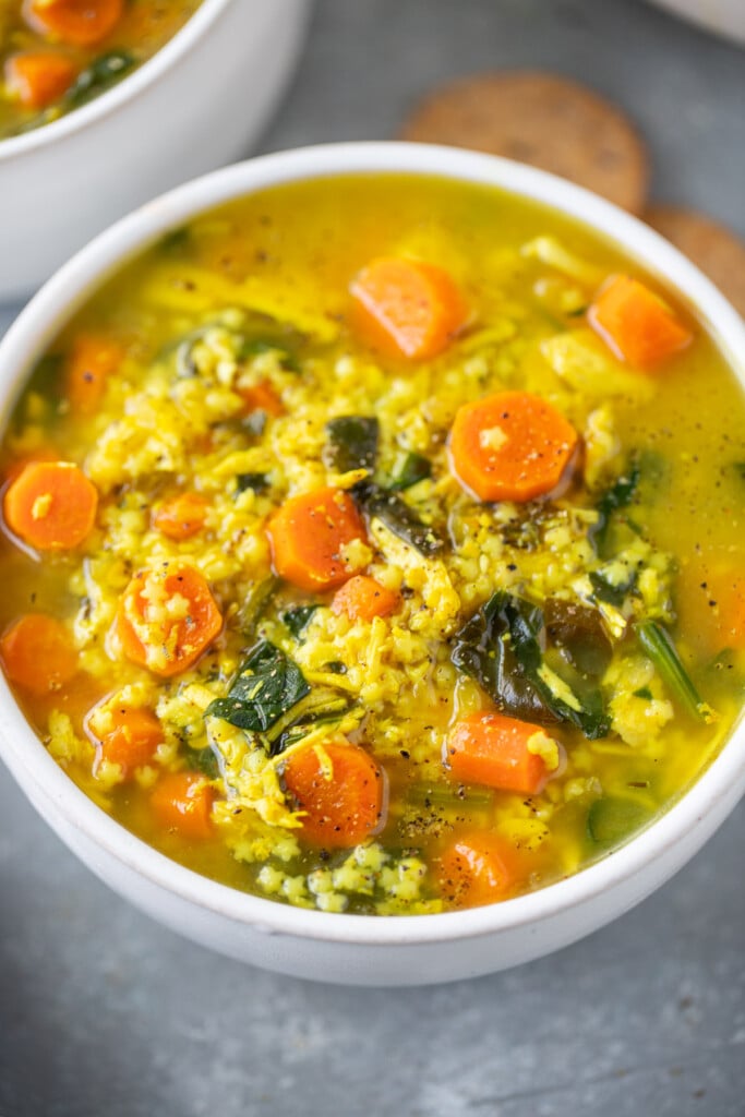Chicken pastina soup in a white bowl on a grey counter with another bowl of soup in the background