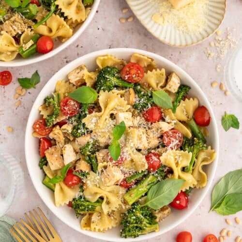 A large bowl of chicken pesto pasta with parmesan cheese, basil pesto, and tomatoes on the side.