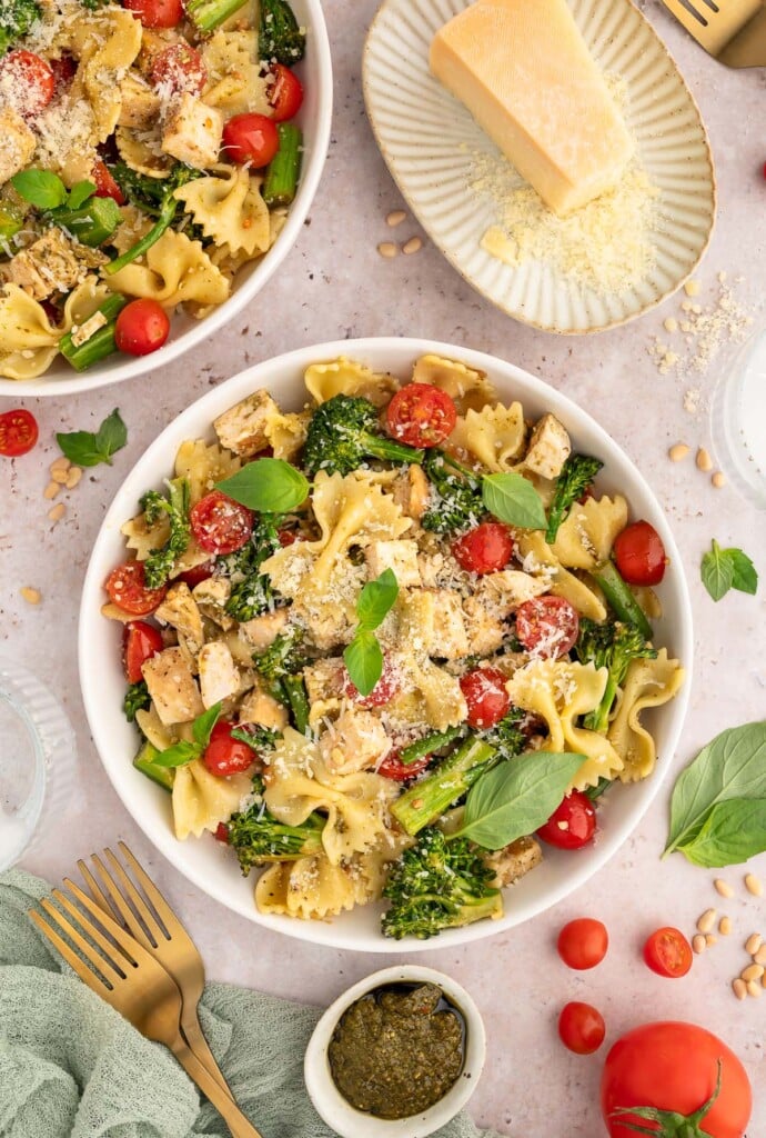 A large bowl of chicken pesto pasta with parmesan cheese, basil pesto, and tomatoes on the side.