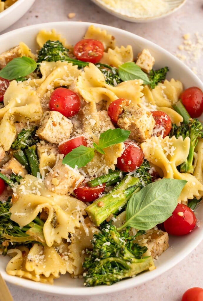 A close up of chicken pesto pasta with tomatoes and broccolini in a white bowl.