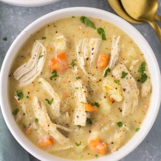 Healthy Chicken Pot Pie Soup in a white bowl on a grey background. Gold spoons are off to the right side