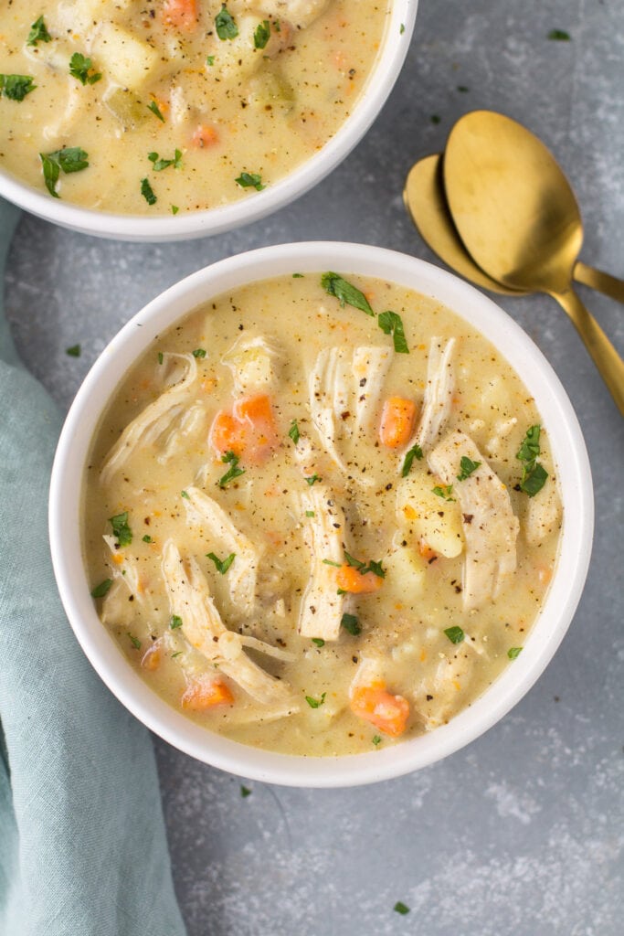 An overhead shot of chicken pot pie soup with black pepper on top in a white bowl on a grey background