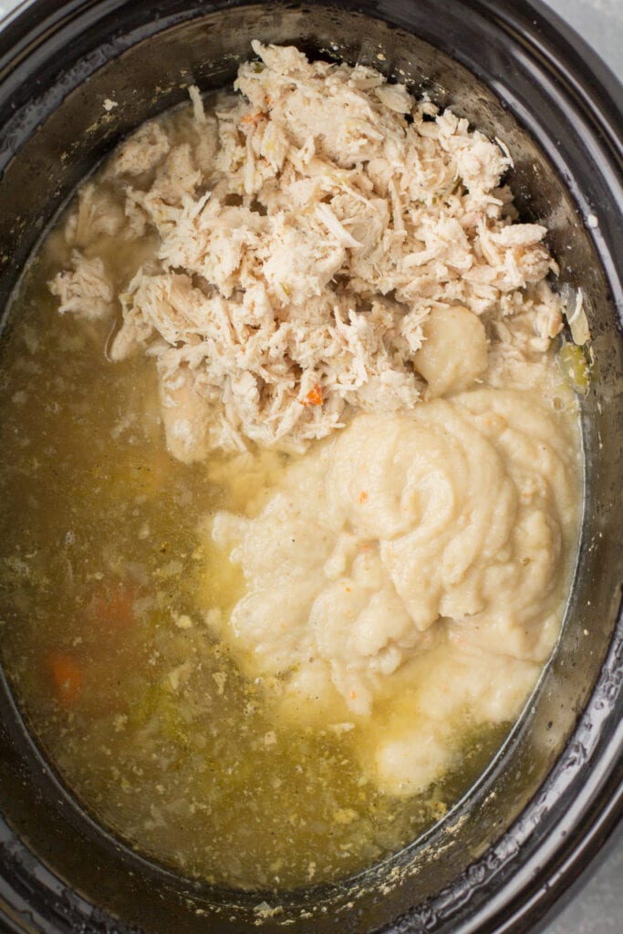 shredded chicken and potatoes being added to a black pot for chicken pot pie soup