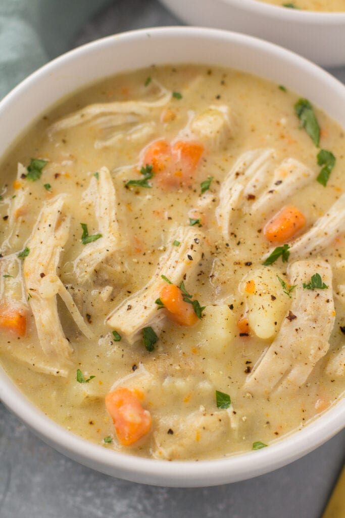 A close up of crockpot chicken pot pie soup with black pepper on top in a white bowl