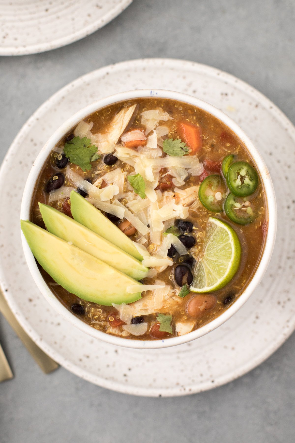 Crockpot Chicken Quinoa Soup in a white bowl garnished with avocado on a white plate with a grey background