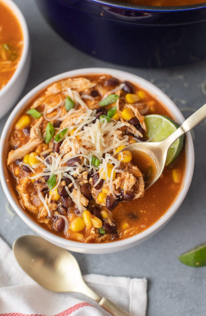 A white bowl of chicken taco soup with a spoon taking a bite out of it