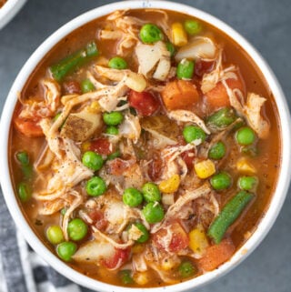 an overhead shot of chicken vegetable soup on a grey background
