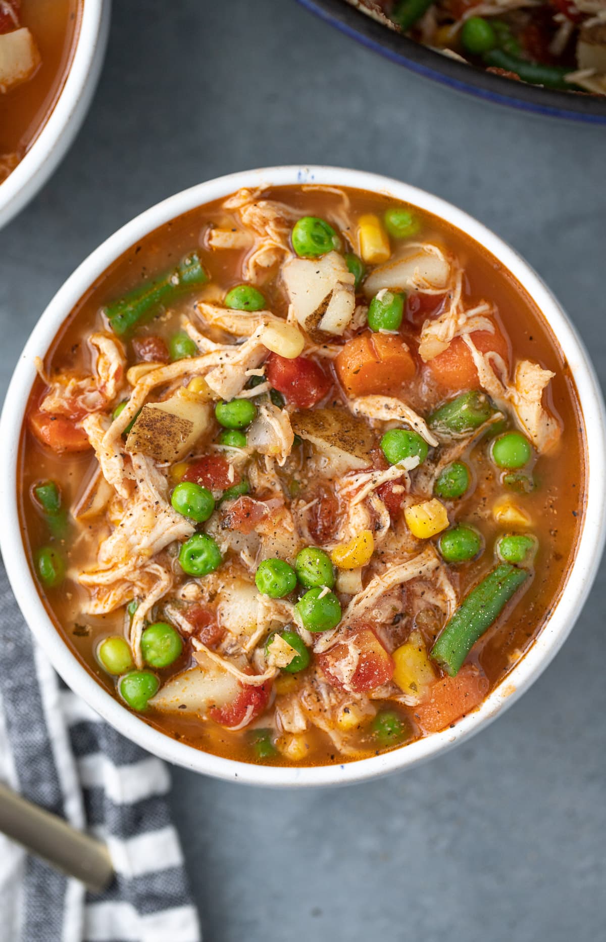 an overhead shot of chicken vegetable soup on a grey background