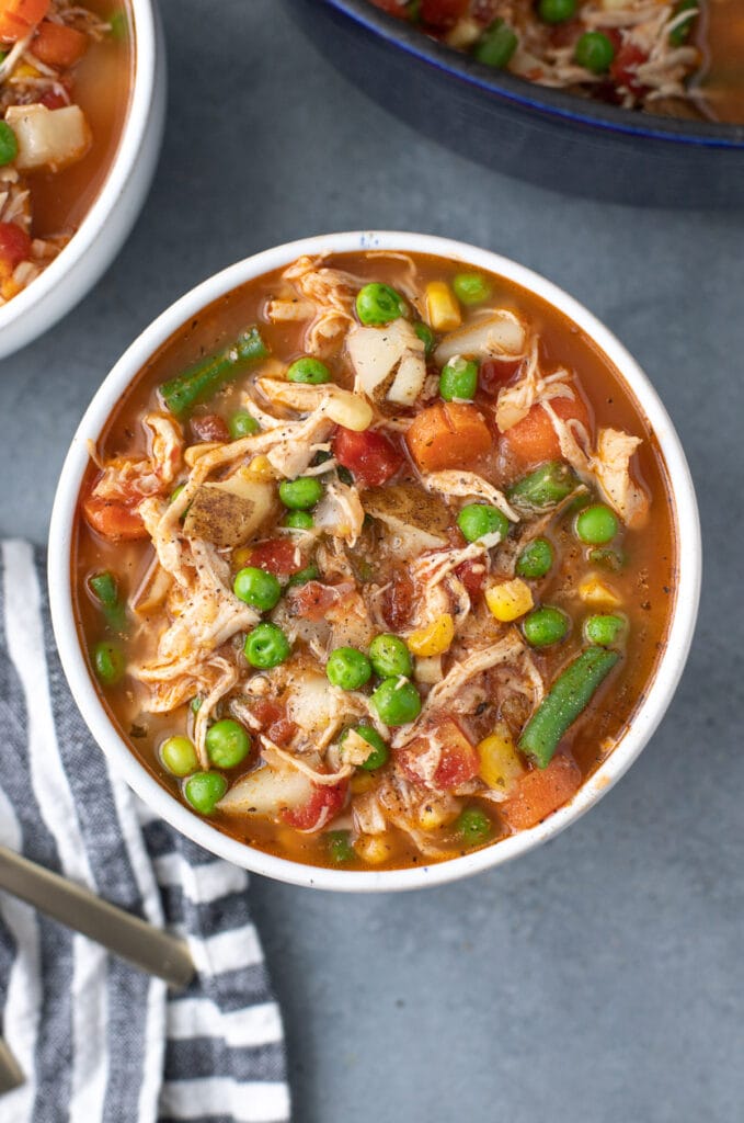 an overhead shot of chicken vegetable soup with another bowl on the side on a grey background