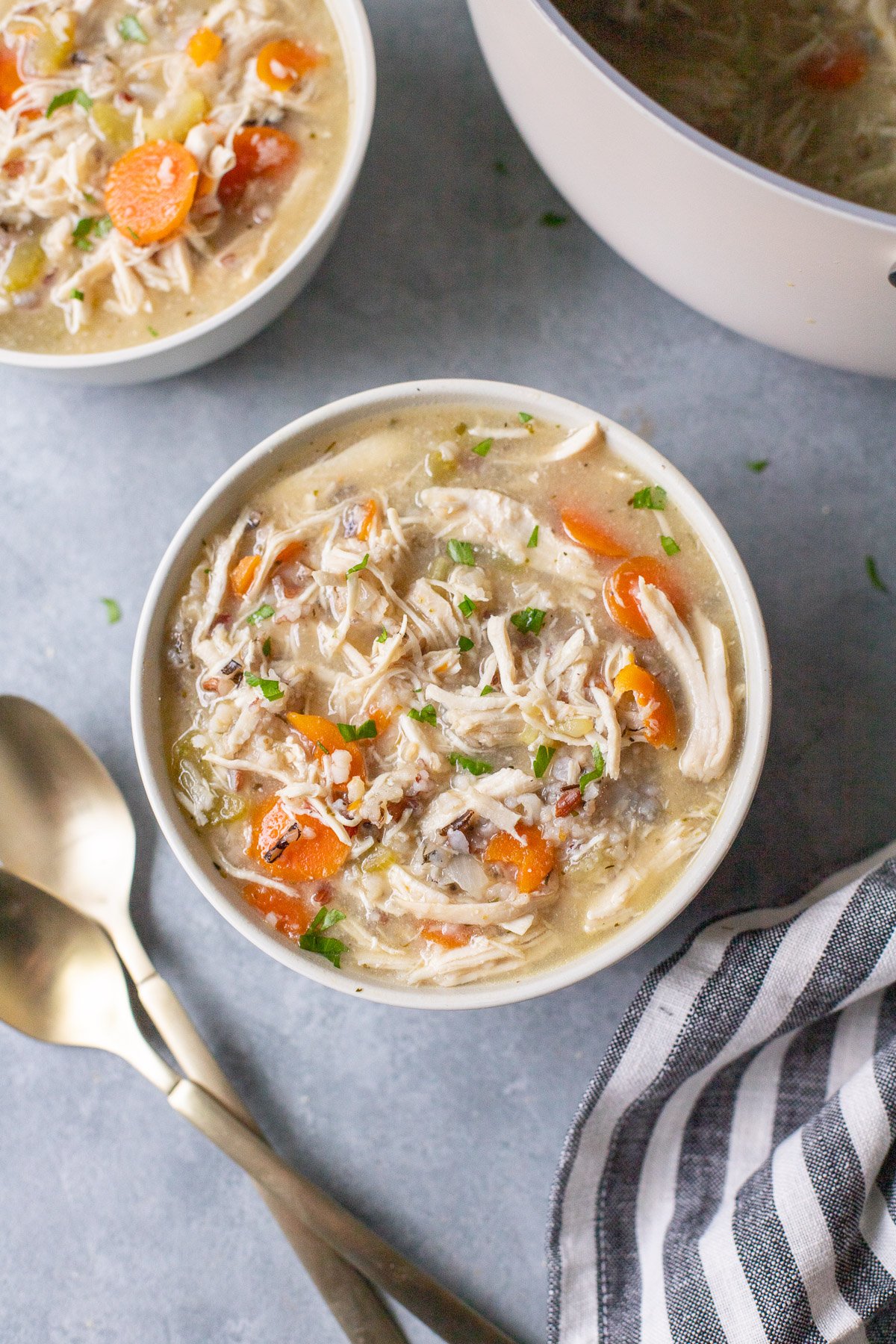An overhead shot of a white bowl of chicken and wild rice soup with another bowl of soup and spoons on the side