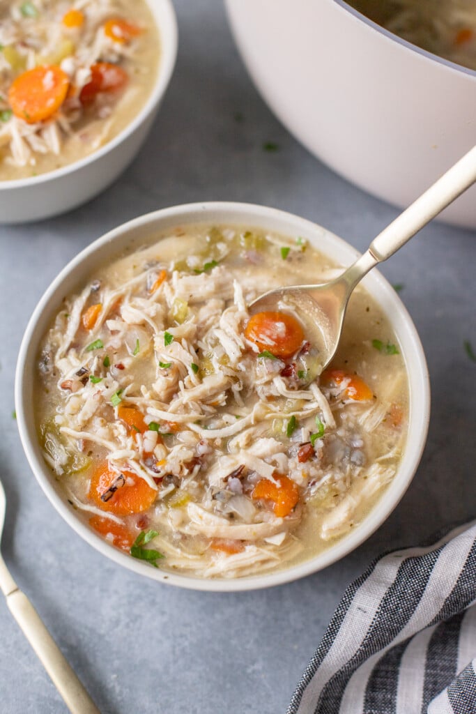 A spoon taking a spoonful of chicken and wild rice soup out of a bowl with another bowl of soup in the background
