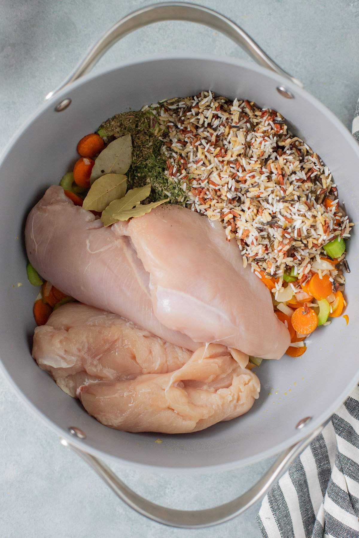 A pot with sauteed veggies, rice, spices, and raw chicken before being cooked for chicken and wild rice soup