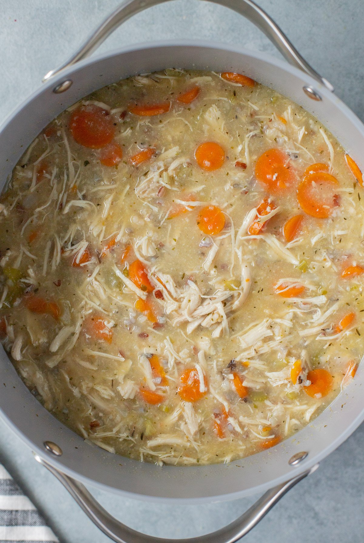 A pot of cooked chicken and wild rice soup on a grey background
