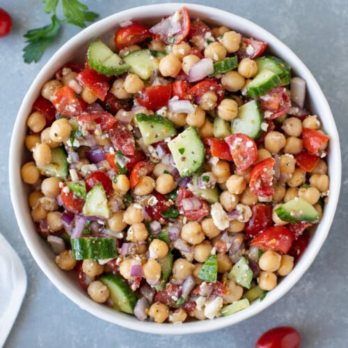 An overhead shot of a white bowl of Mediterranean chickpea salad on a grey background