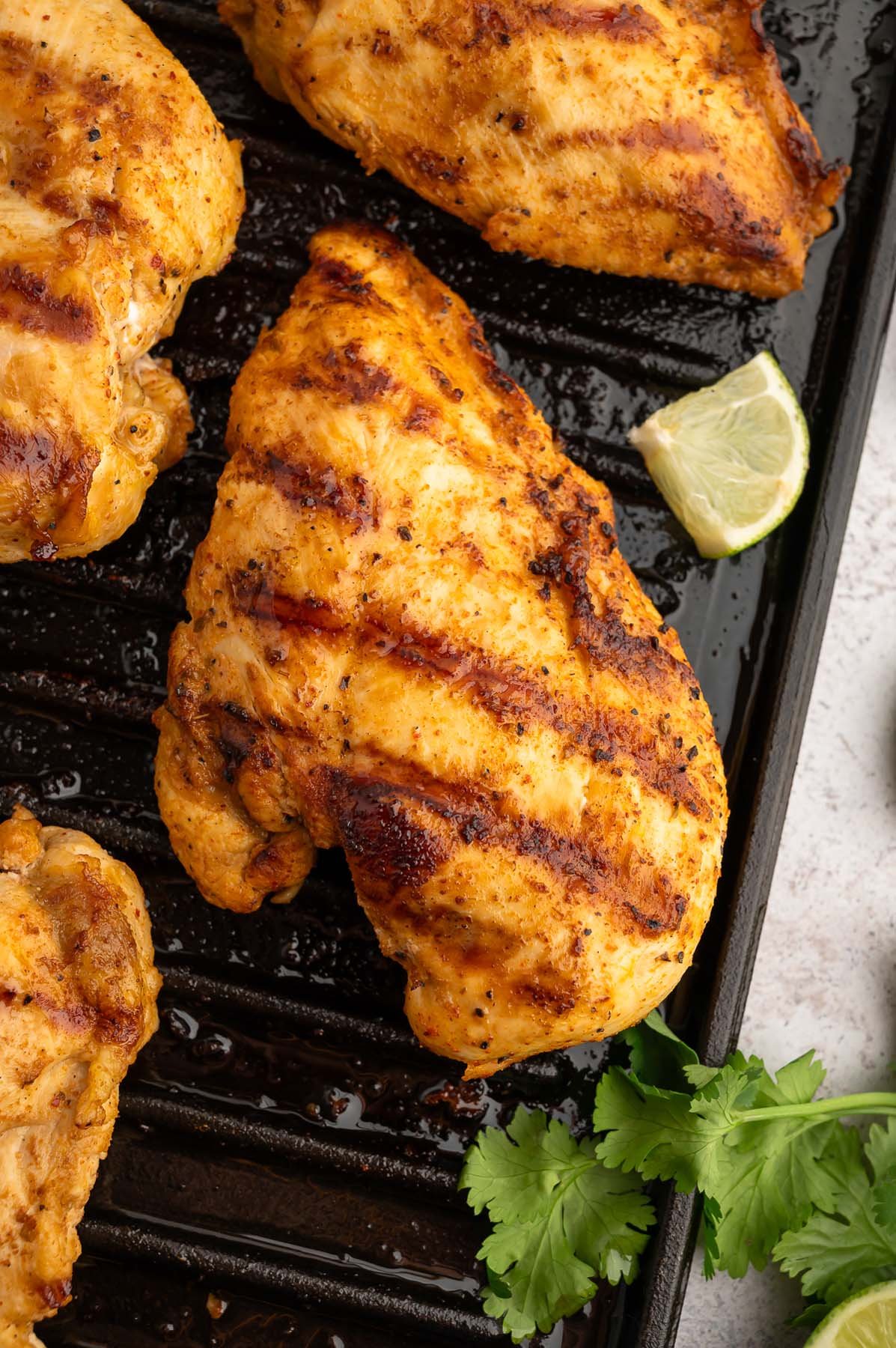 Chili Lime Chicken Breasts on a cast iron grill with a lime slice and cilantro on the side.