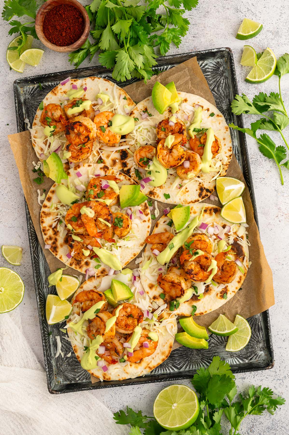 5 Chili Lime Shrimp Tacos on a black sheet pan with chili powder, limes, and cilantro on the side.