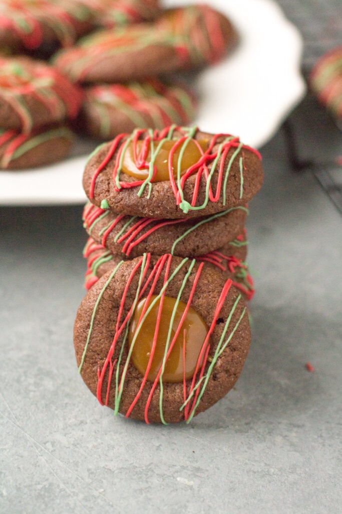 A stack of Chocolate Caramel Thumbprint Cookies on a grey background