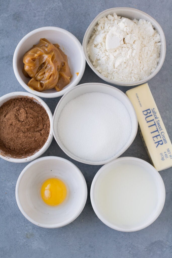 Ingredients for Chocolate Caramel Thumbprint Cookies in small white bowls on a grey background