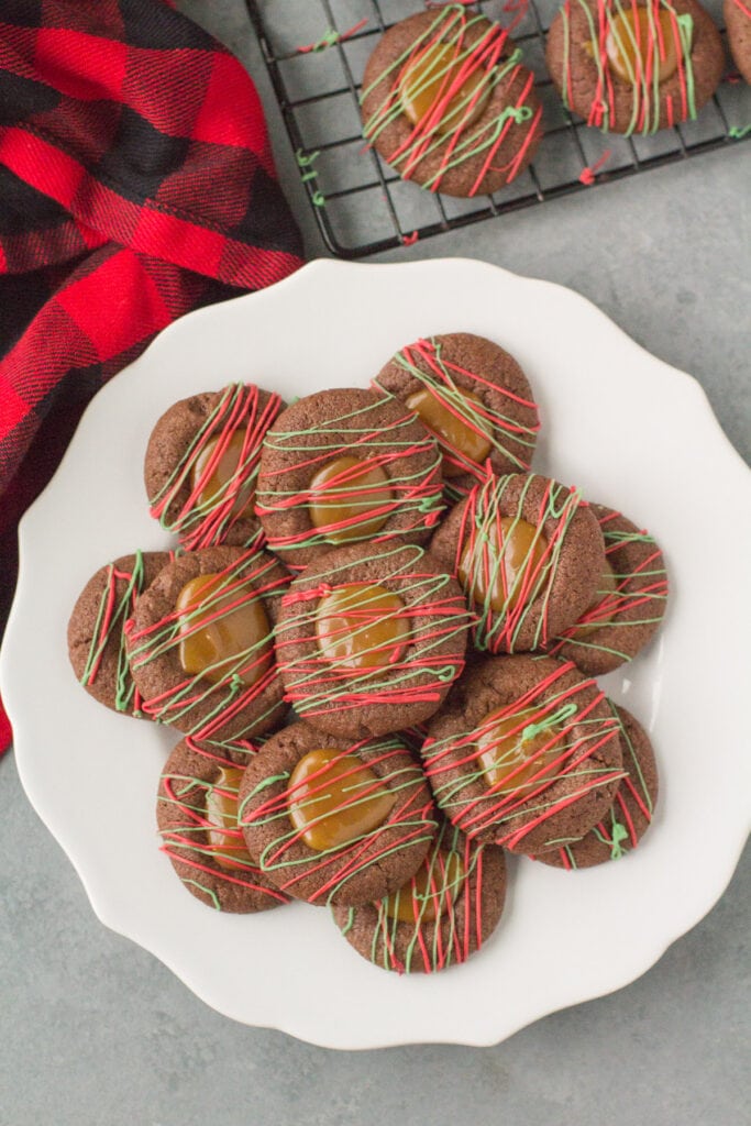 Chocolate Caramel Thumbprint Cookies on a white plate with a cooling rack and red linen off to the side