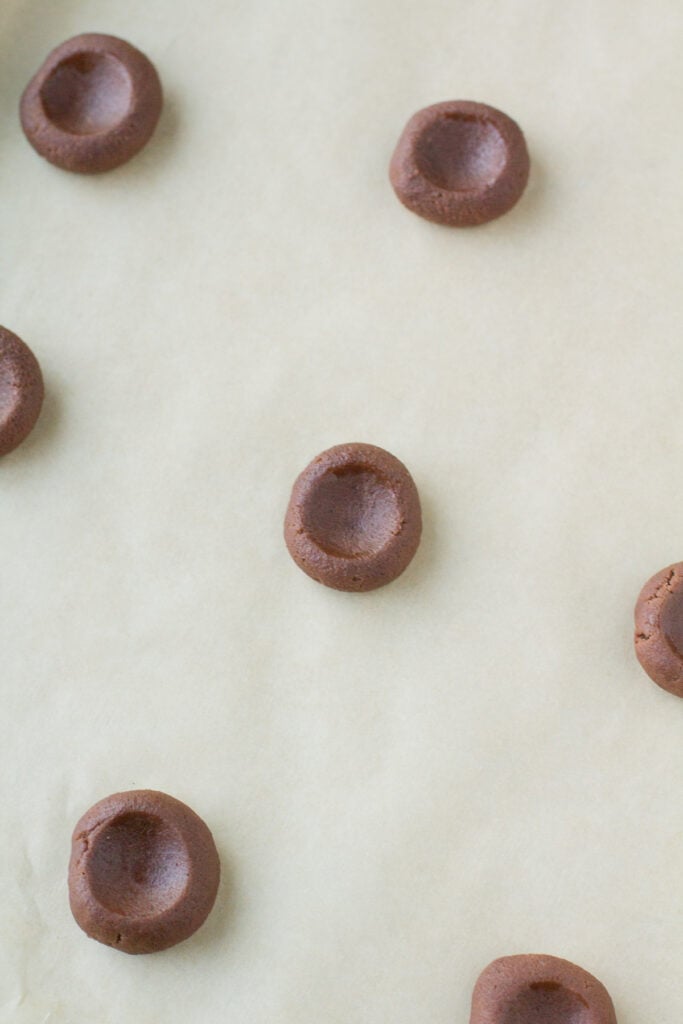 dough balls for chocolate caramel thumbprints on a parchment lined baking sheet with an indent made into them