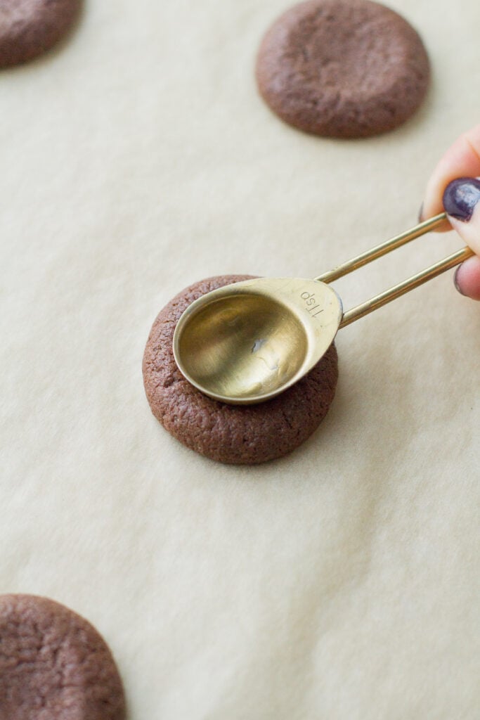 a teaspoon pressing into chocolate caramel thumbprint cookies to make an indent