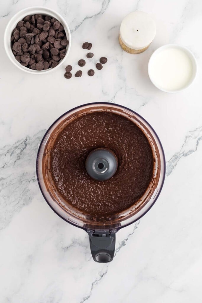 Chocolate dessert hummus in a food processor after blending with a bowl of chocolate chips on the side.