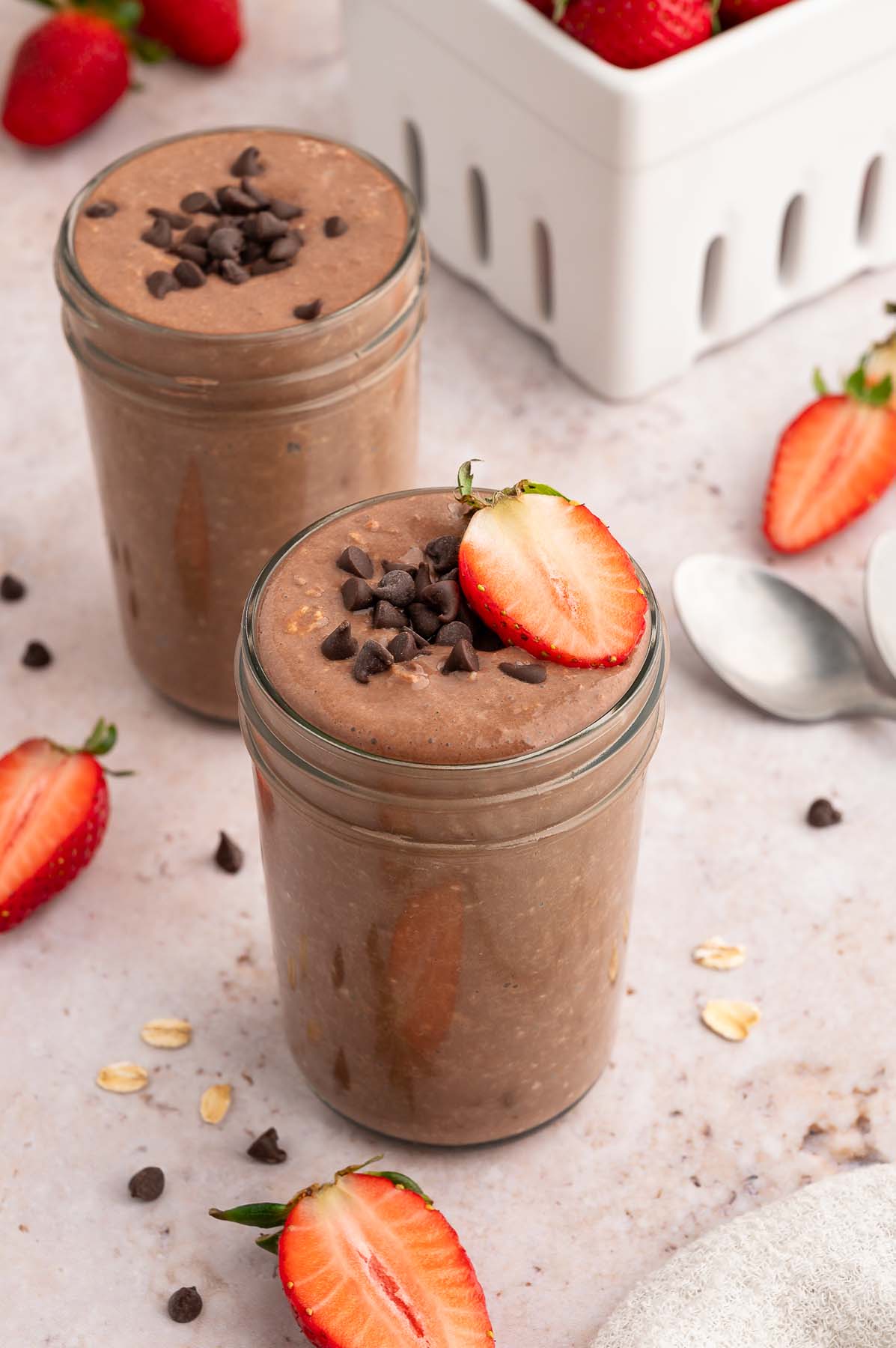 Two mason jars with chocolate overnight oats topped with mini chocolate chips and sliced strawberries.