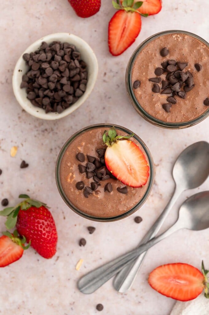 An overhead shot of two mason jars with chocolate overnight oats topped with mini chocolate chips and sliced strawberries.