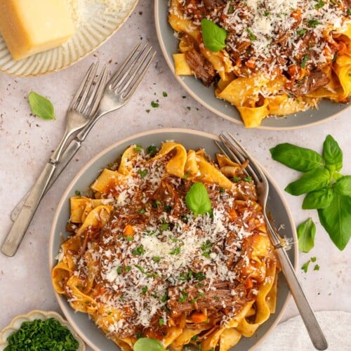 Two plates of chuck roast pasta topped with cheese and fresh herbs with forks on the side.
