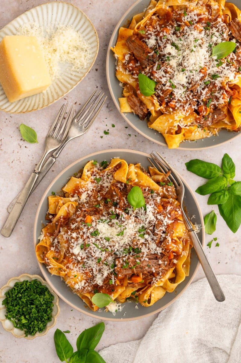 Two plates of chuck roast pasta topped with cheese and fresh herbs with forks on the side.