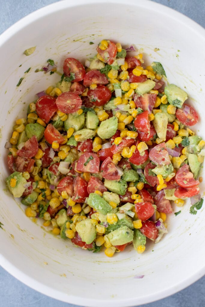 A close up of Corn Tomato Avocado Salad mixed together in a mixing bowl
