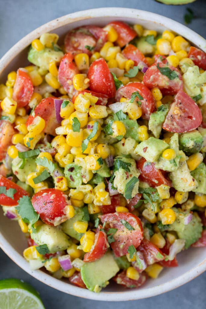 A close up of corn avocado and tomato salad in a small white bowl
