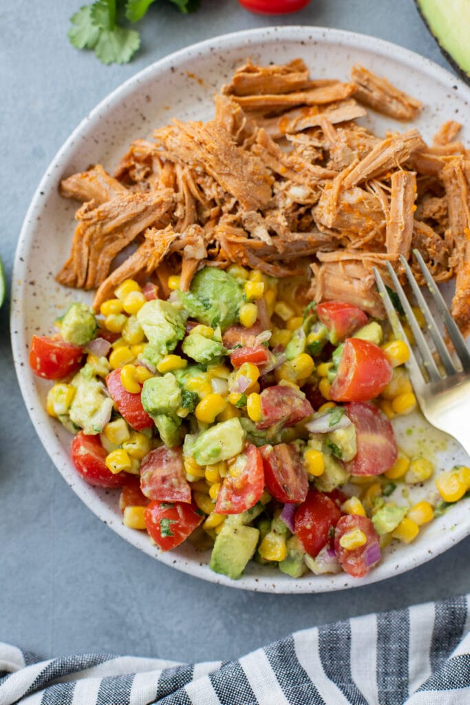 Corn Tomato Avocado Salad on a white plate with pulled pork and a fork off to the side