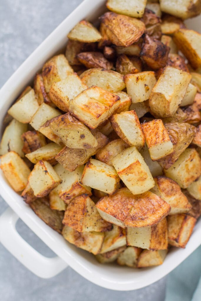 A white serving bowl filled with crispy roasted potatoes.