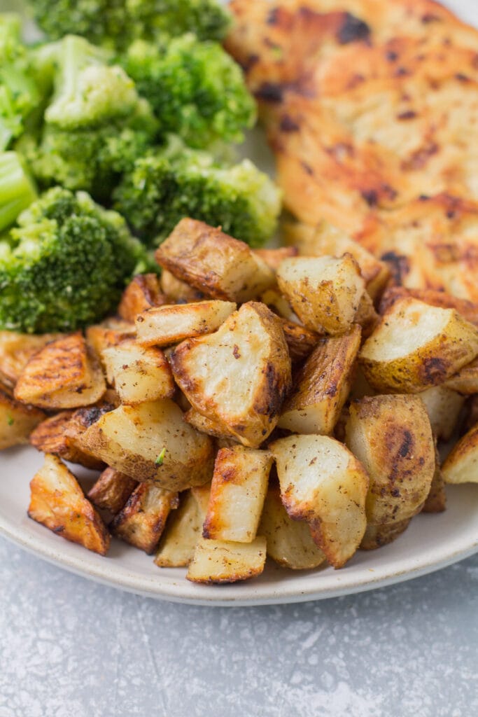 A plate piled high with roasted russet potatoes, chicken + broccoli