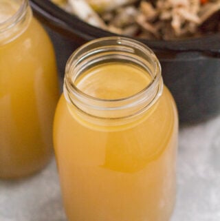 A glass of bone broth in front of a crockpot
