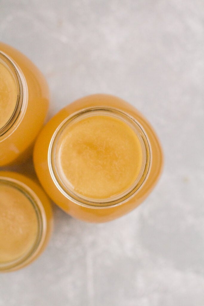 an overhead shot of bone broth in glass mason jars. it's a light yellow color, and swirling at the top