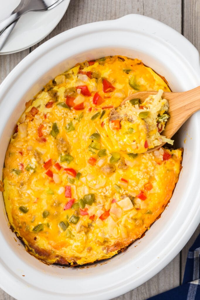 Crock pot breakfast casserole in the crockpot with a wooden spoon taking a scoop out