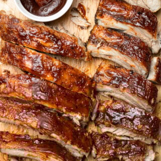 an overhead shot of crock pot baby back ribs in two rows with a white bowl of bbq sauce on the side