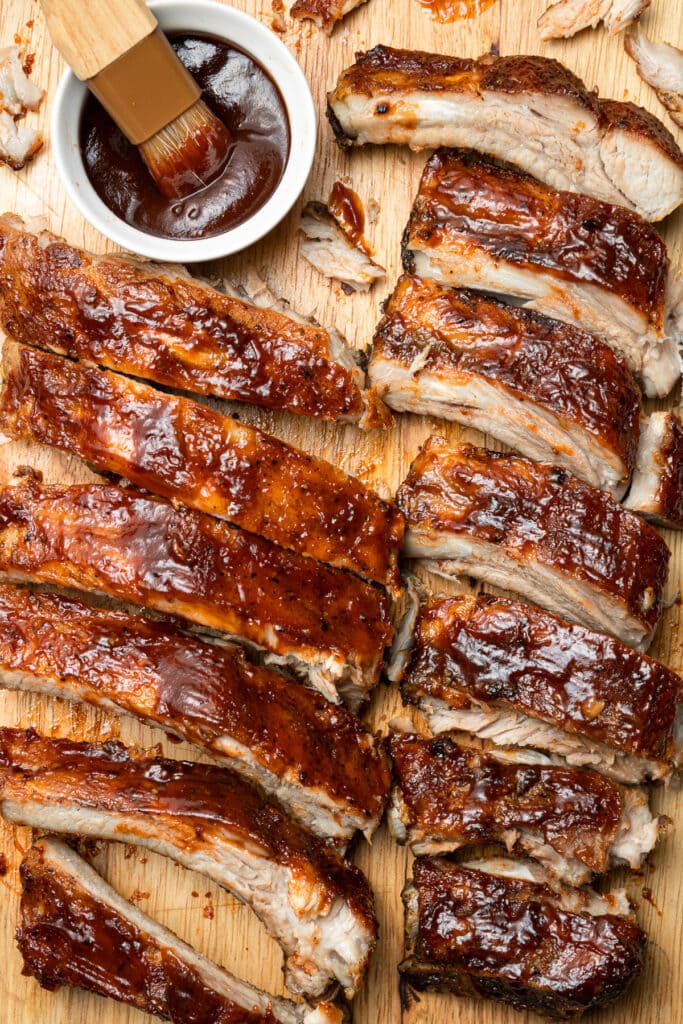 an overhead shot of crock pot baby back ribs in two rows with a white bowl of bbq sauce on the side