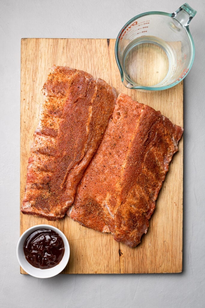 slow cooker ribs coated in dry rub spices with bbq sauce and water on the side