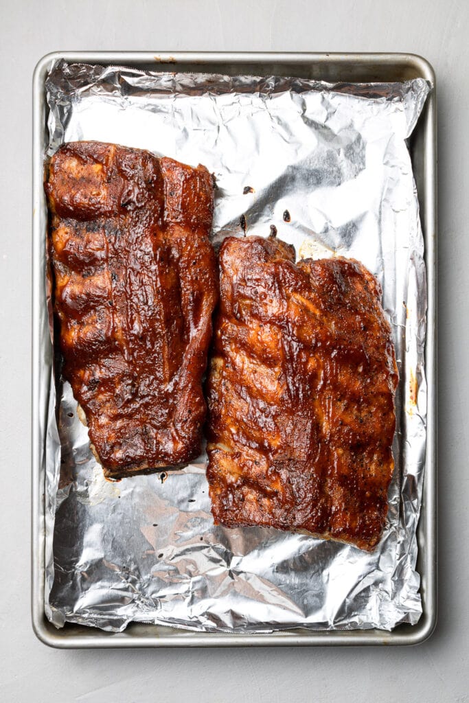 crockpot baby back ribs on a sheet pan covered in bbq sauce