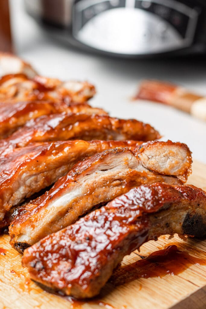a close up shot of crock pot baby back ribs with a slow cooker in the background