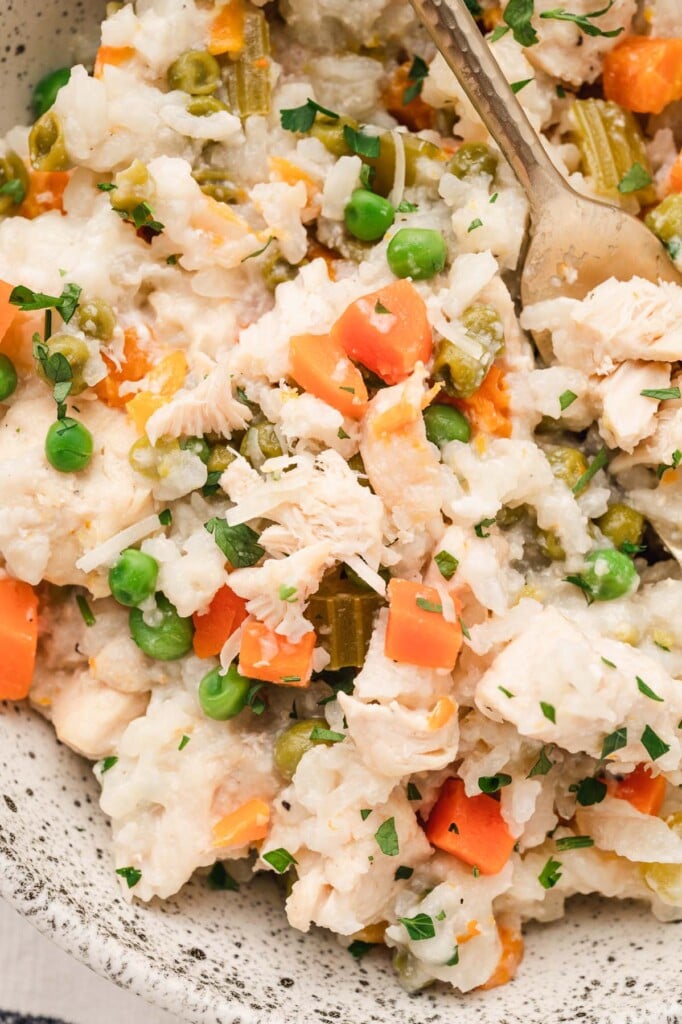 A close up of crockpot chicken and rice in a bowl with a gold spoon in it. 