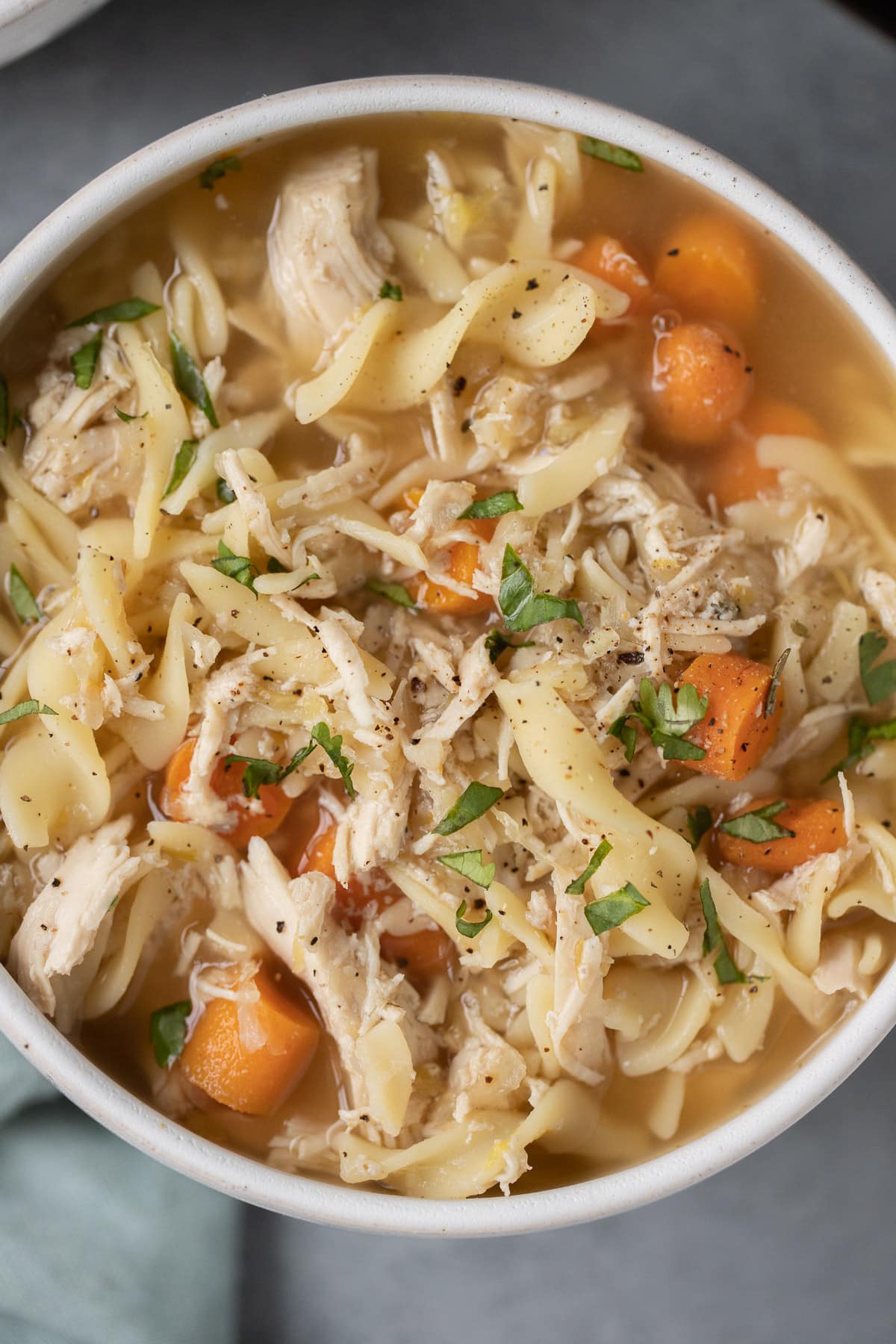 A close up of crockpot chicken noodle soup in a white bowl on a grey background