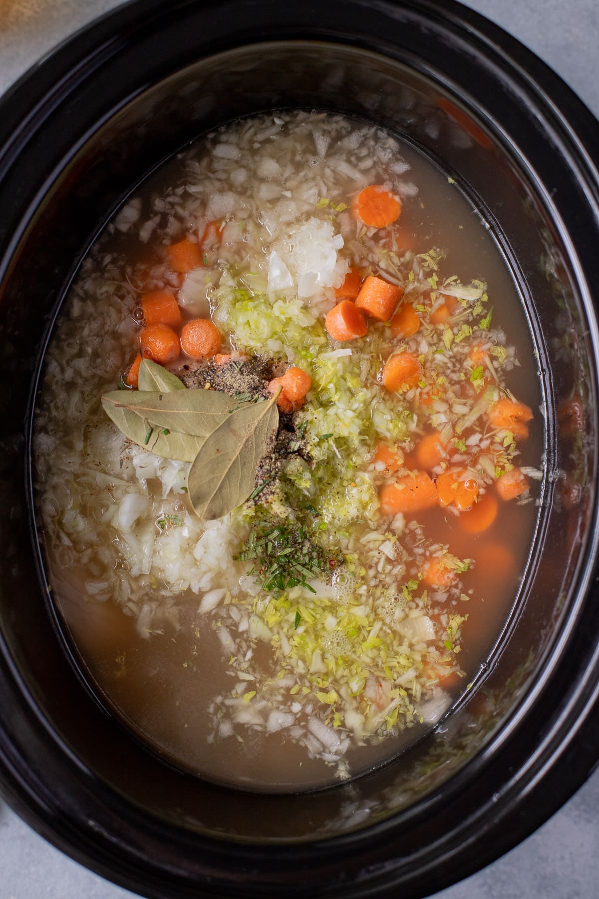 A collage showing How to Make Crockpot Chicken Noodle Soup- raw in a black crockpot base before cooking
