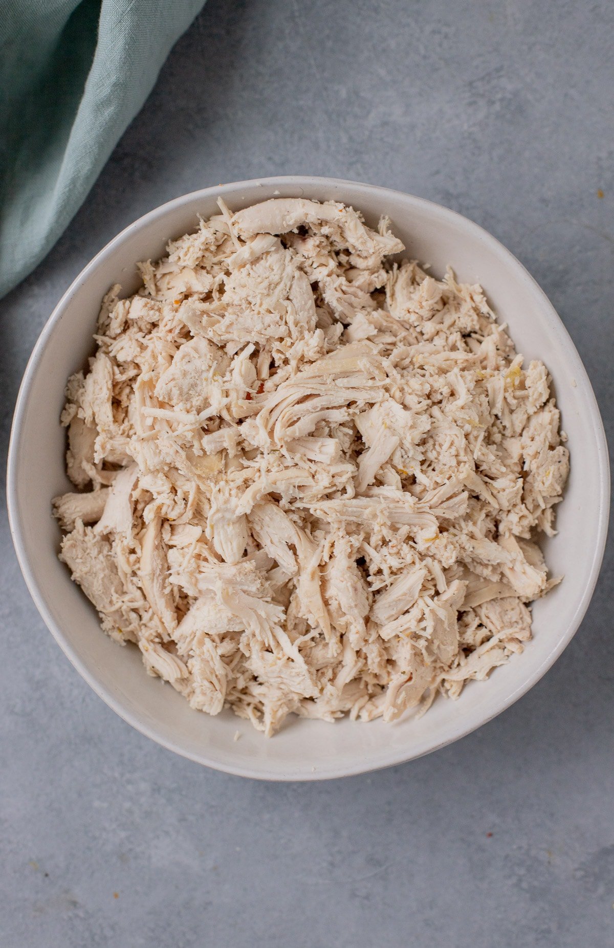 Chicken shredded for crockpot chicken noodle soup in a white bowl on a grey background