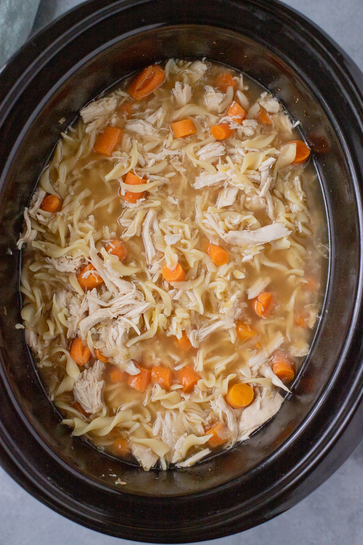 A close up of one pot crockpot chicken noodle soup in a black crockpot base